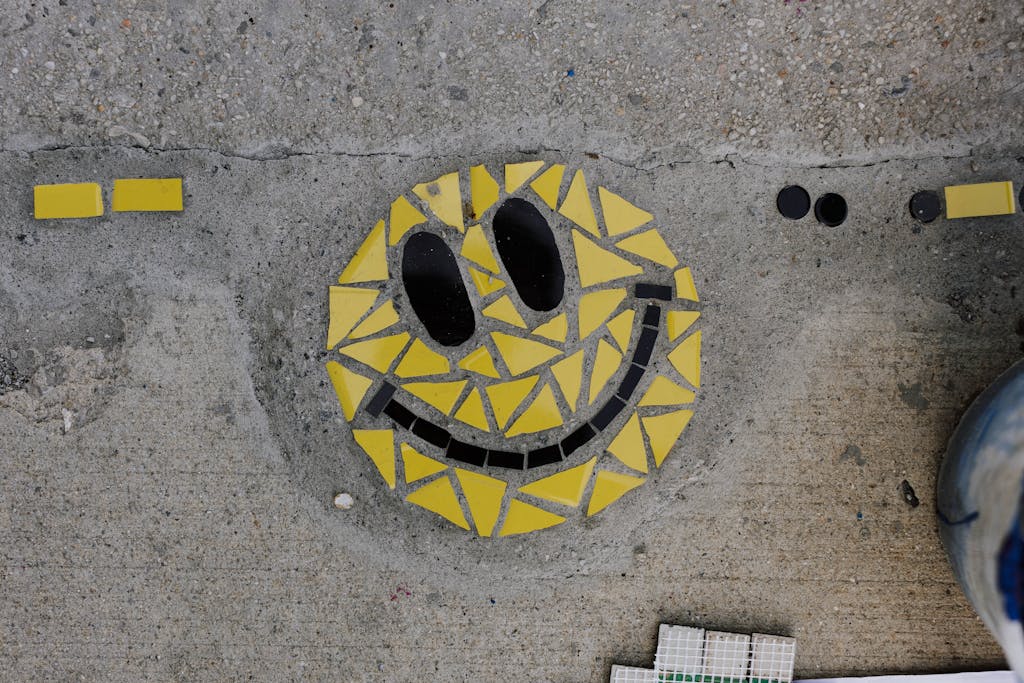 Concrete sidewalk featuring a vibrant yellow mosaic smiley face art piece.